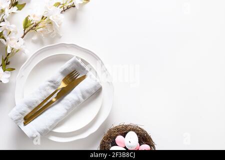 Spring Easter dinner decorated eggs in nest and blossom flowers on white table. View from above. Copy space Stock Photo