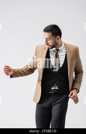 young muslim man looking at sleeve of trendy blazer while posing isolated on grey Stock Photo