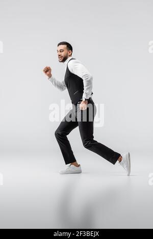 full length view of young arabian man in fashionable clothes and sneakers running on grey Stock Photo