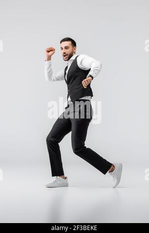 full length view of excited arabian man in fashionable clothes dancing on grey Stock Photo