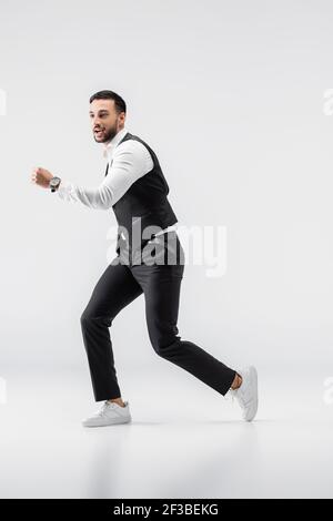 full length view of fashionable arabian man looking away while running on grey Stock Photo