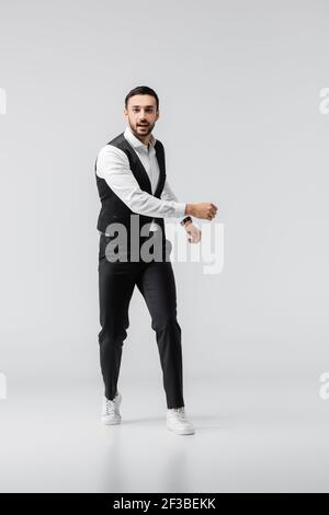 full length view of young, trendy arabian man looking at camera while running on grey Stock Photo