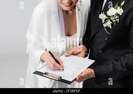 Cropped view of smiling bride signing wedding contract near groom isolated on grey