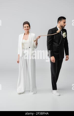 Happy young woman holding slip knot near muslim groom on white background Stock Photo