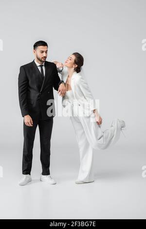 Happy bride standing near arabian groom in handcuffs on white background Stock Photo