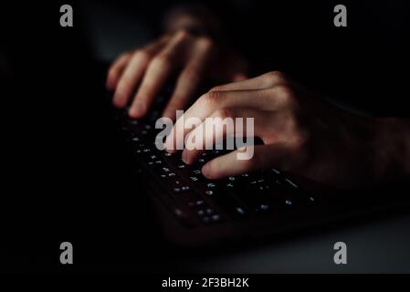 Close up man hand typing keyboard on laptop in darkness operating room, cyber security concept. Hacker using laptop. Stock Photo