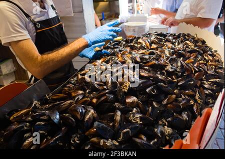 Heap of mussels in shells stuffed with rice and served with lemon. Man selling midye traditional Turkish food in Midyeci Ahmet cafe. Istanbul, Turkey. Stock Photo