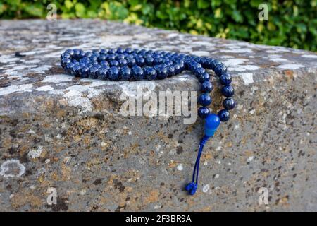 Close up of blue mala beads (lapis lazuli) on stone with green leaves in  the background. Mindfulness and meditation accessory Stock Photo - Alamy