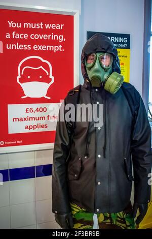 Man in Gas Mask in Chislehurst Station in front of You must wear a face covering unless exempt sign, protecting himself from the pandemic Stock Photo