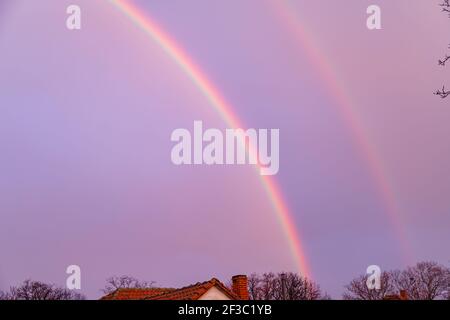 A double rainbow over the roofs of rural houses Stock Photo