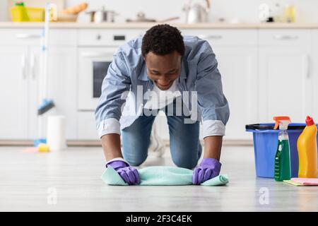 Hard-working black guy cleaning floor in kitchen Stock Photo