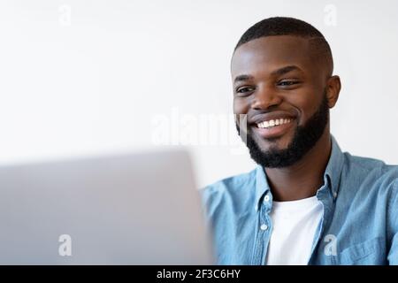 Closeup Shot Of Smiling Young Black Man Using Laptop Stock Photo