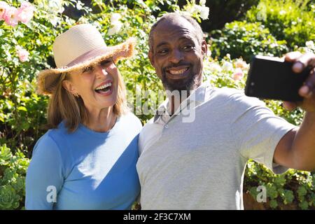 Diverse senior couple in garden taking selfie with smartphone Stock Photo