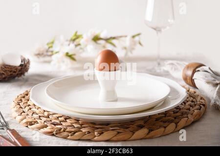 Easter table setting with organic egg in stand, bunny and spring blossom flowers. Decorative serving of natural materials. Festive religion traditiona Stock Photo