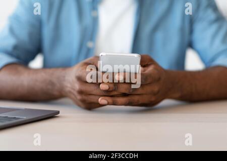 Closeup Shot Of African American Man Sitting At Desk And Using Smartphone Stock Photo
