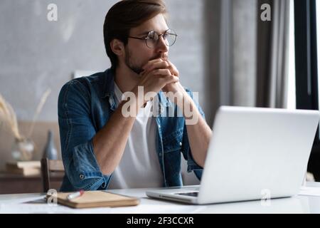Thoughtful man looking away while sitting at his working place in office Stock Photo