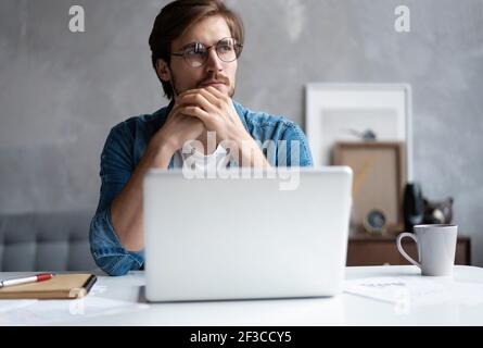 Thoughtful man looking away while sitting at his working place in office Stock Photo