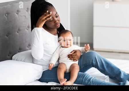 Tired African American mom sitting with kid on bed Stock Photo