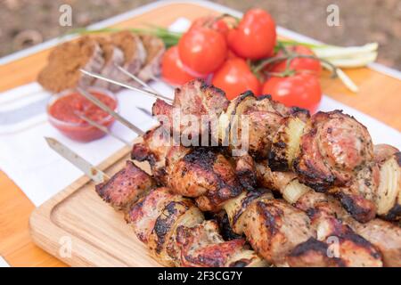 Pork shish kebabs on skewers with fresh vegetables, on a wooden background. Barbecuing lunch Stock Photo