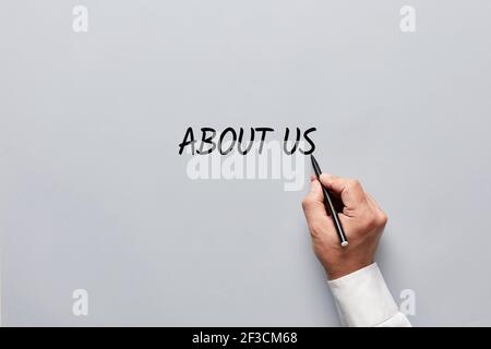 Male hand writing the word about us on gray background. Promoting the company or business publicity concept. Stock Photo
