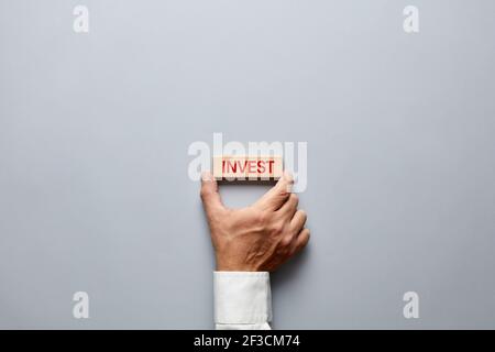 Businessman hand holding a wooden block with the word invest on it. Decision of financial investment in business concept. Stock Photo