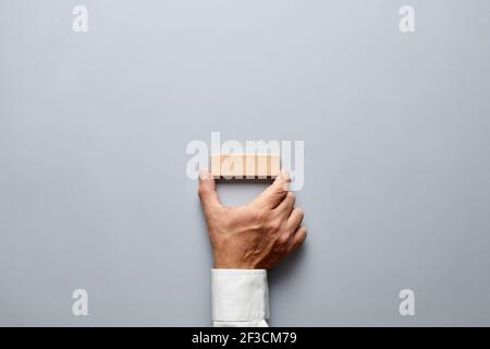 Businessman hand holding a blank or empty wooden block on gray background. Stock Photo