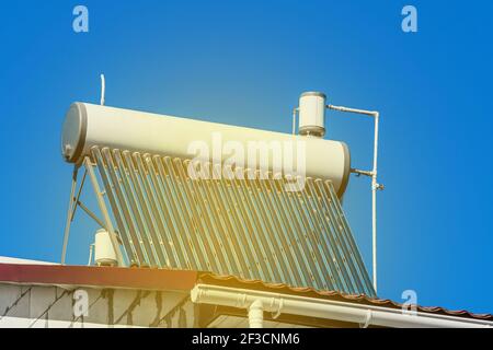 Solar water heater on the roof of a building against the background of the blue sky. Using solar panels energy to heat water. Stock Photo