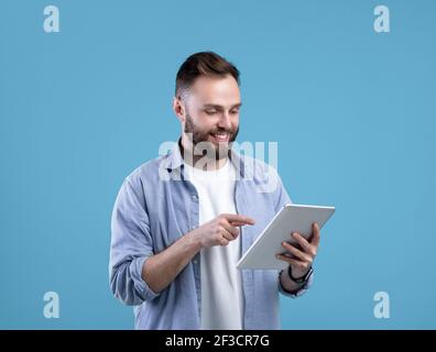 Joyful bearded man using tablet computer for online work or studies on blue studio background Stock Photo