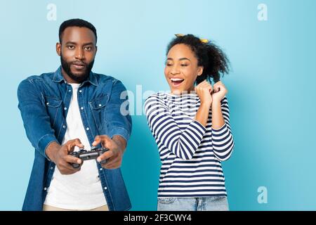 KYIV, UKRAINE - OCTOBER 23, 2020: amazed african american woman looking at husband gaming on blue Stock Photo