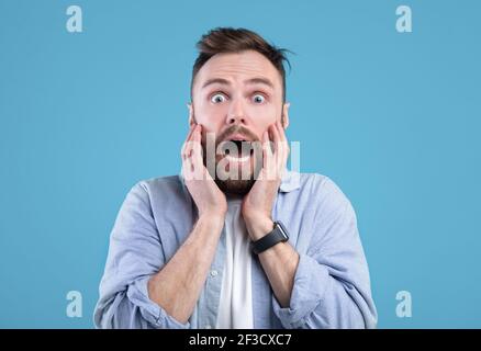 Scared young guy screaming in panic over blue studio background Stock Photo