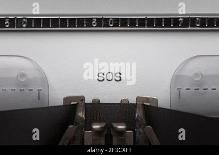 Typing text SOS on vintage manual typewriter. Close up of writes word on white paper. Typing a Morse code distress signal - The phrase save our souls. Stock Photo