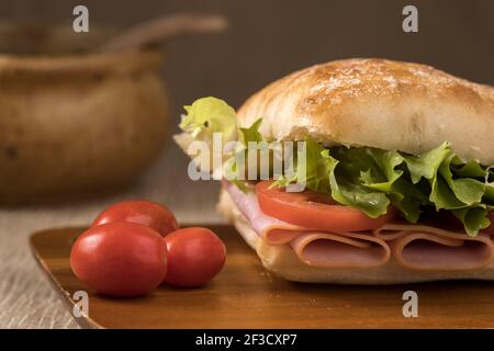A close up photo of a ham sandwich with ciabatta bread, lettuce, and tomatoes on a cutting board. Stock Photo