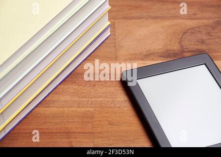 Student desk, pile of books and electronic reader with blank screen on a wooden surface. Concepts of technology, reading and education. Stock Photo