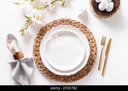 Easter dinner with eggs, bunny, festive tableware and blooming flowers on white table. Top view. Stock Photo