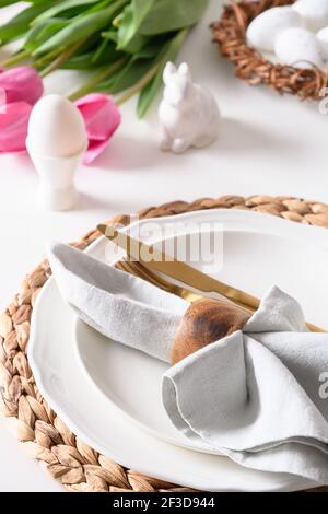 Easter dinner with egg in stand, bunny and tulips on white table. Close up. Stock Photo