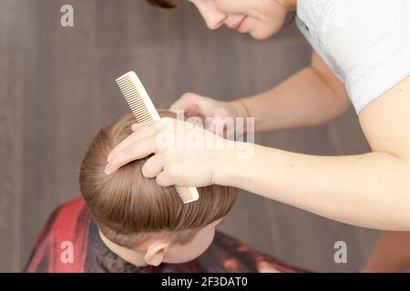 young mom hairdresser cuts her baby boy at home with hair clipper during quarantine. selective focus. portrait Stock Photo