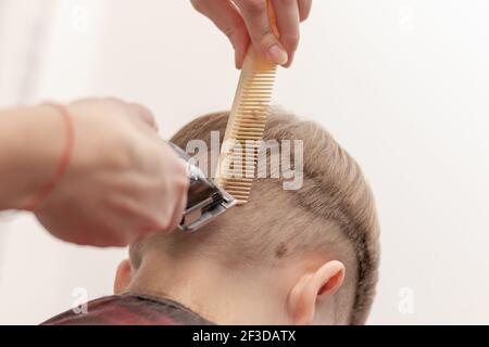 a woman's mother's hands are neatly cut with a comb and clipper for her child at home at the back. selective focus close-up Stock Photo