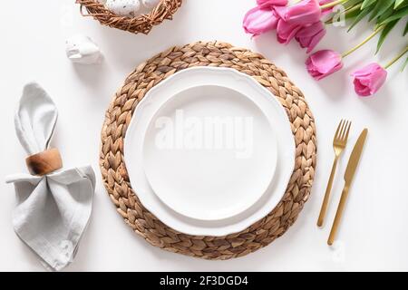 Easter dinner with eggs, bunny, festive tableware and tulips on white table. Top view. Stock Photo