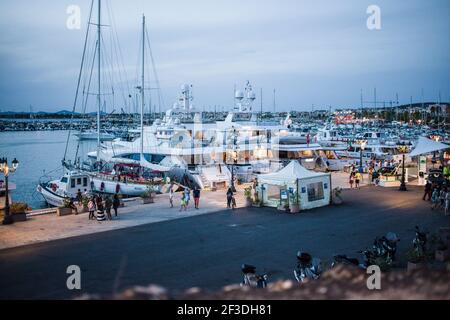 Port of Alghero at dusk in Sardinia. The marina has a number of different nautical vessels docked for the evening. Many luxury yachts, and boats. Stock Photo