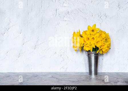 A bouquet of daffodils in a vase against white plastered wall with copy space. Stock Photo