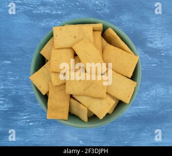Top view Cheese and garlic snack crackers in a green bowl on a blue painted wood background. Stock Photo