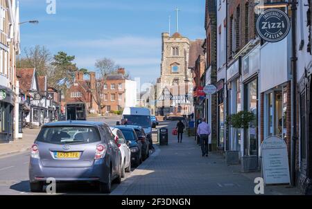 Pinner Village high street with shops, St John the Baptist Parish Church, parked cars and a few people walking on the pavement. NW London, England Stock Photo