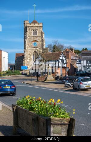 Pinner Village high street with medieval hilltop church St John the Baptist, flower box of daffodils, war memorial & historic half-timbered buildings. Stock Photo