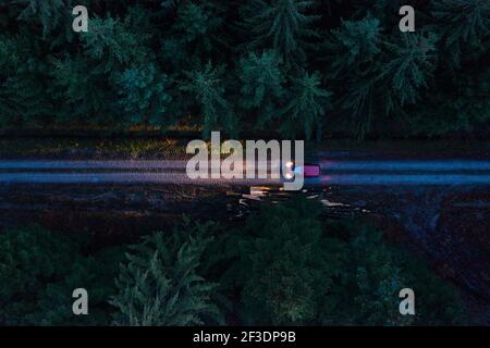 Top down aerial shot of a single red car on a dirt road at night, in an alpine european forest. Dramatic with only the headlights. lelab360 Stock Photo