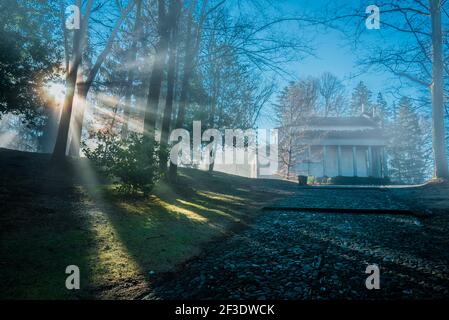 Path through park forest uphill to historic religion landmark. Rays of bright morning sun shining through trees. Stock Photo
