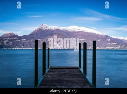 Panoramic view on snow capped mountain ridge. Wooden lookout pier above lake water surface in foreground.