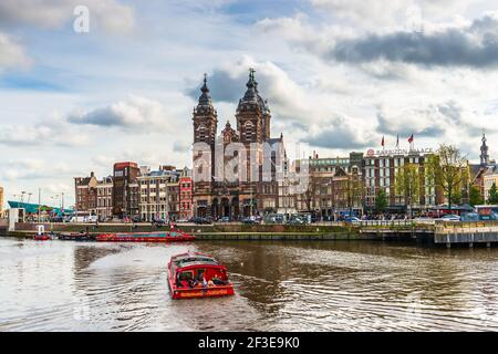 View of St. Nicholas Church main catholic church in the city, and boat traffic on the Amstel in Amsterdam in Holland, Netherlands Stock Photo