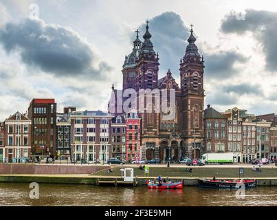 View of St. Nicholas Church main catholic church in the city, and boat traffic on the Amstel in Amsterdam in Holland, Netherlands Stock Photo