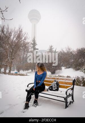Girl with curly hair sitting and posing on the bench under the snow in the botanical park Stock Photo