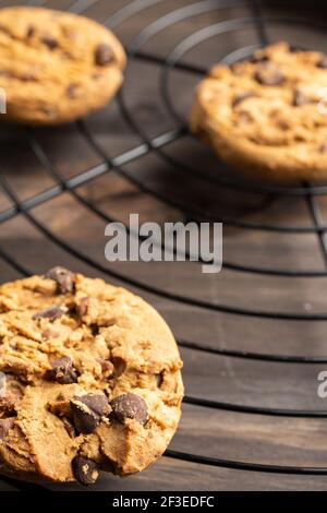 Top view of three chocolate chip cookies on wire rack, selective focus, on wooden table, vertical Stock Photo